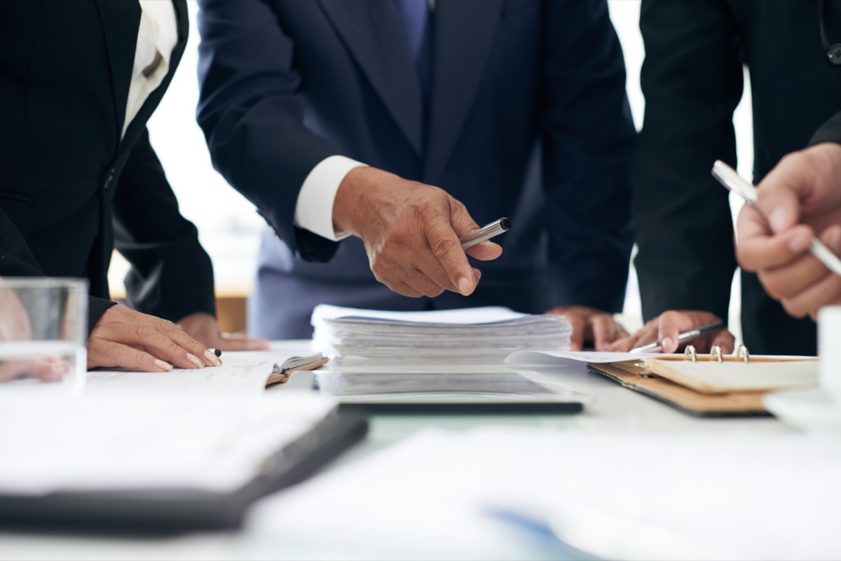 Attorneys in suits reviewing stacks of documents together at a conference table.