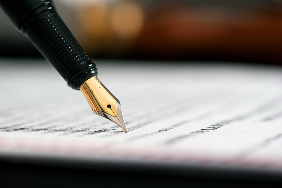 A gold-nibbed fountain pen signing a printed legal document.